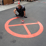 Bild:Mitarbeiter malt den Kreis und die Umrandung der Halteverbot-Markierung mit roter Farbe